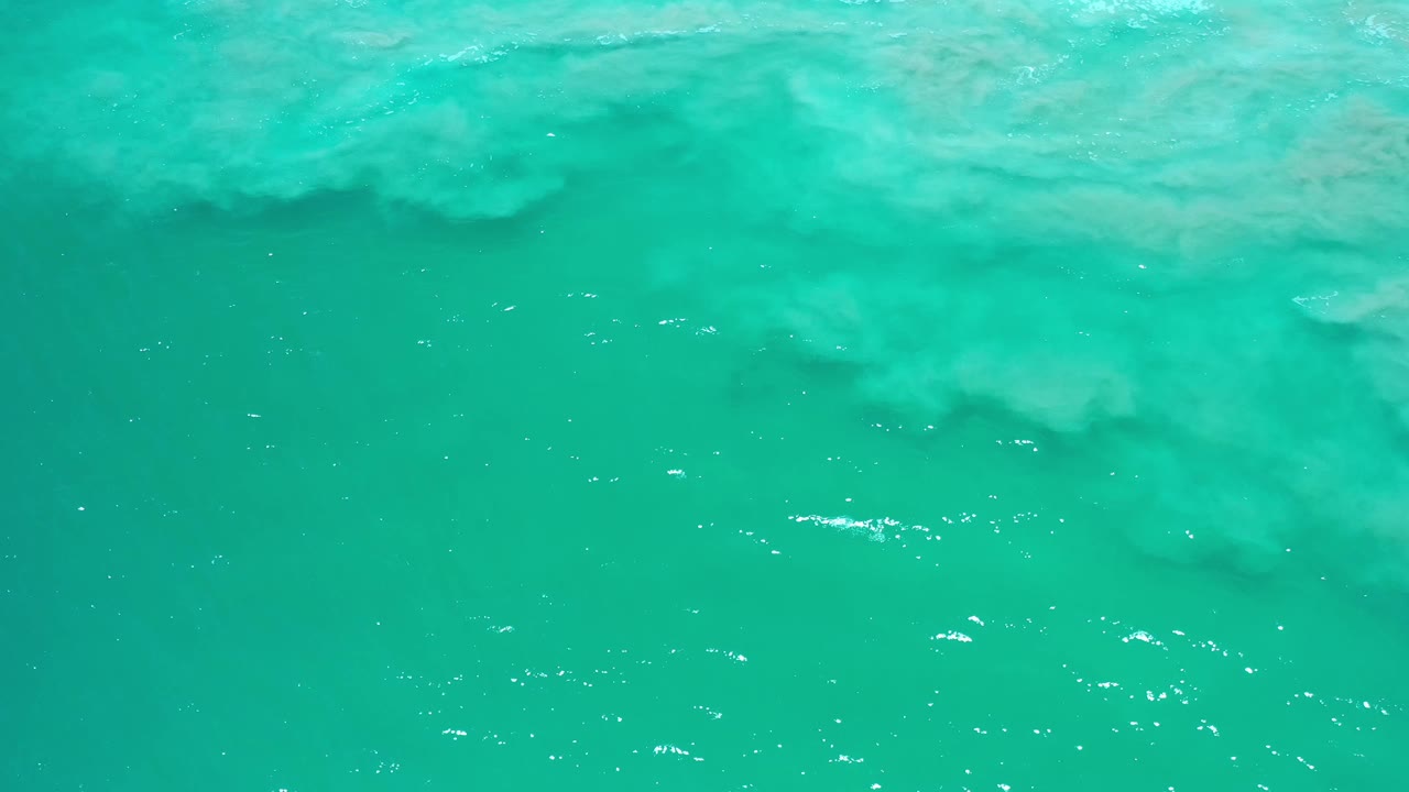 Clear Los Cabos water fills the frame, with a broader pale sand shape near the upper edge and no visible people.