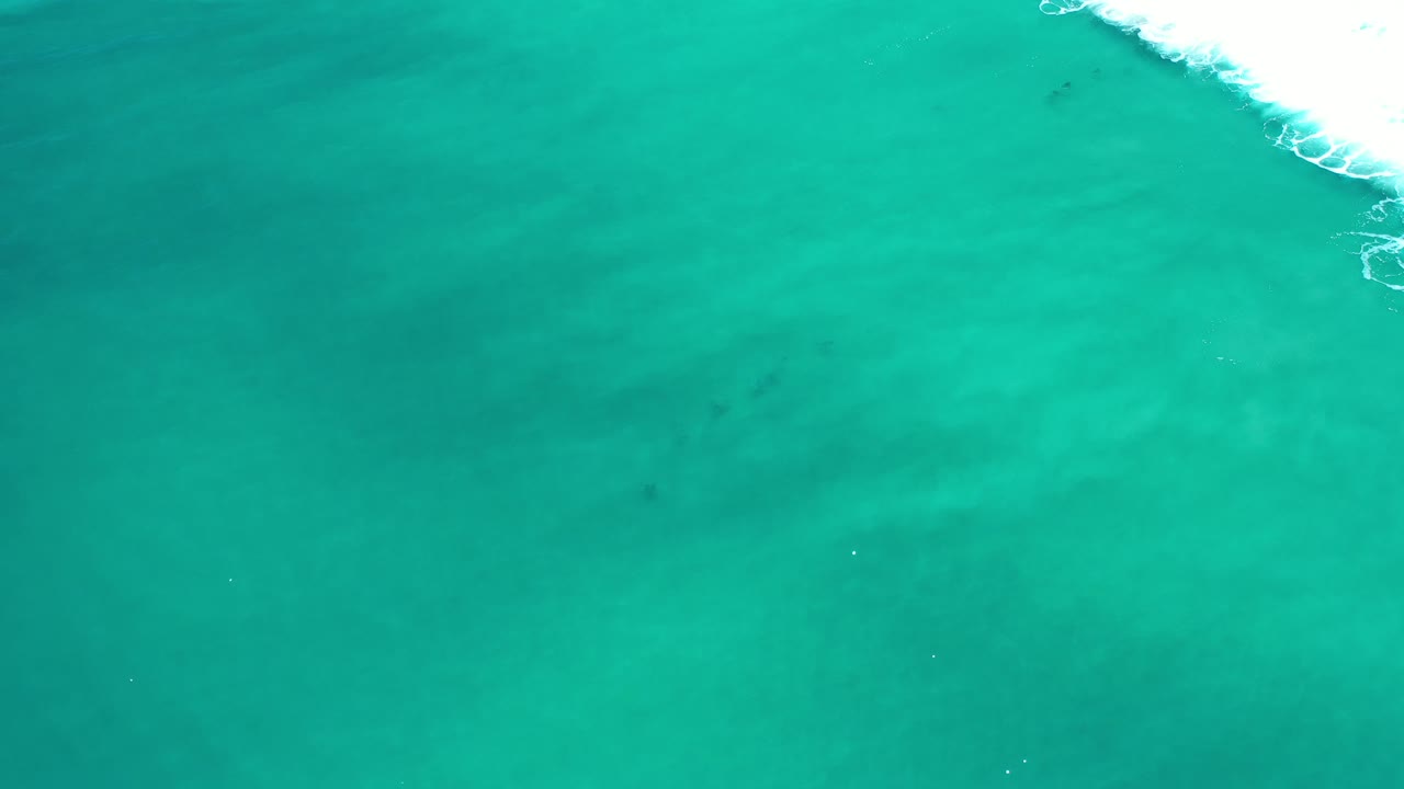Turquoise sea surface with foam along the upper right
