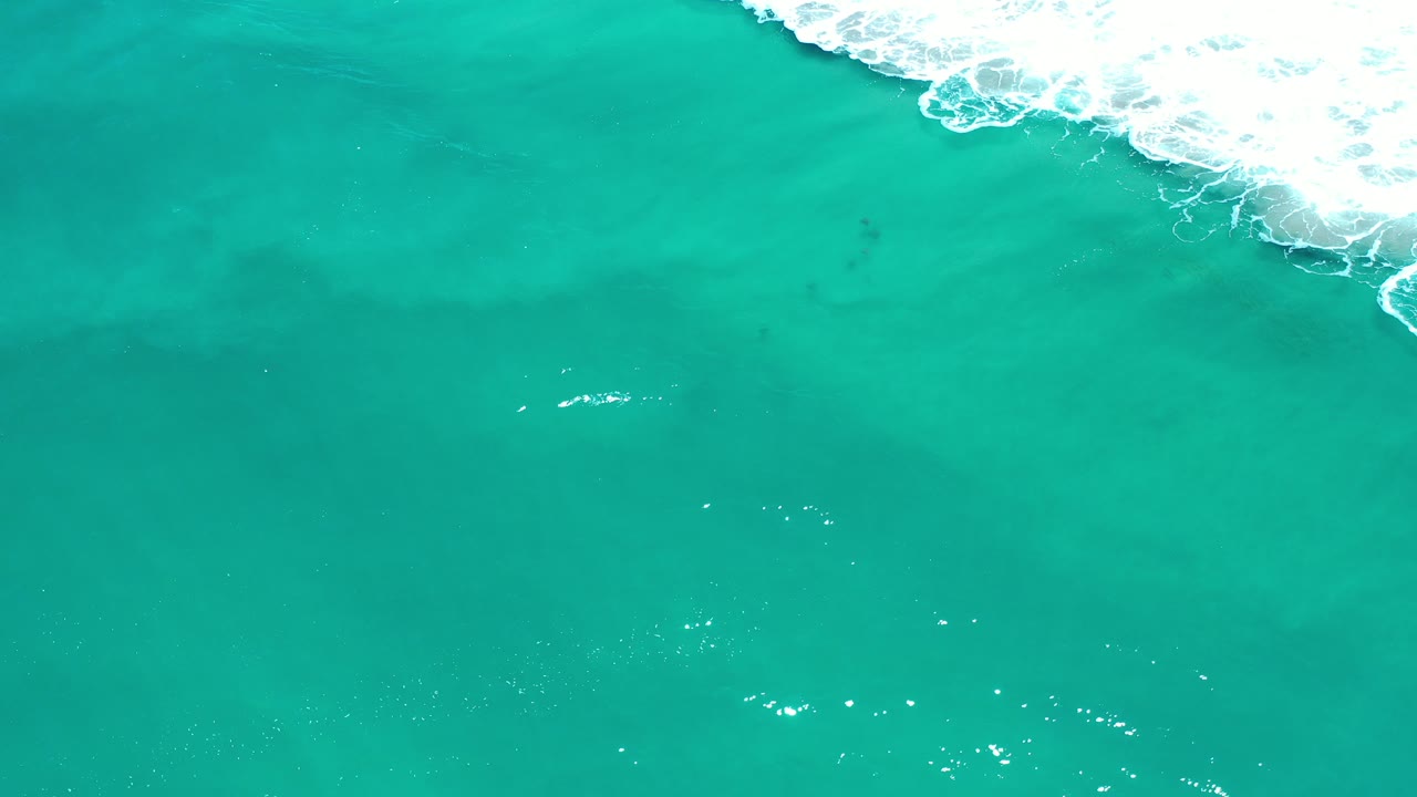 Overhead view of turquoise-green ocean in Los Cabos, Mexico, with white surf entering from the upper right and no visible people.