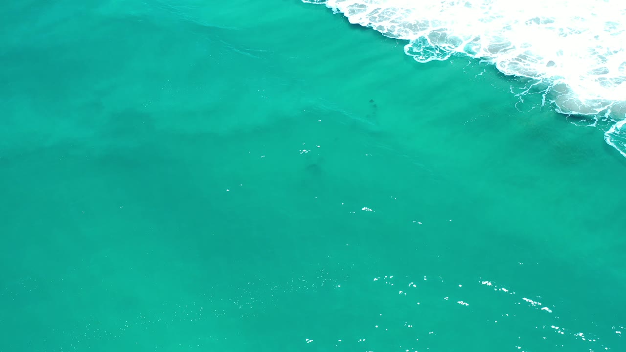 Clear green water with surf breaking along the upper right.
