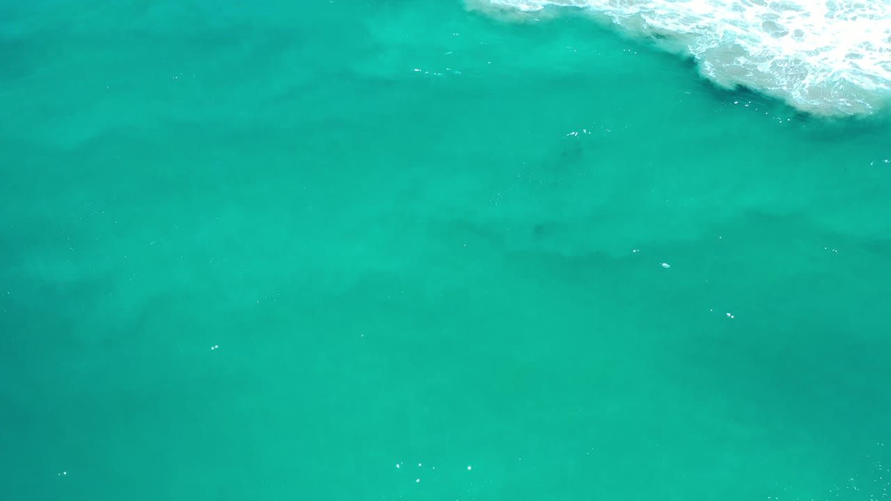 Overhead view of turquoise ocean water in Los Cabos, Mexico, with white surf cutting in from the upper right and no visible people.