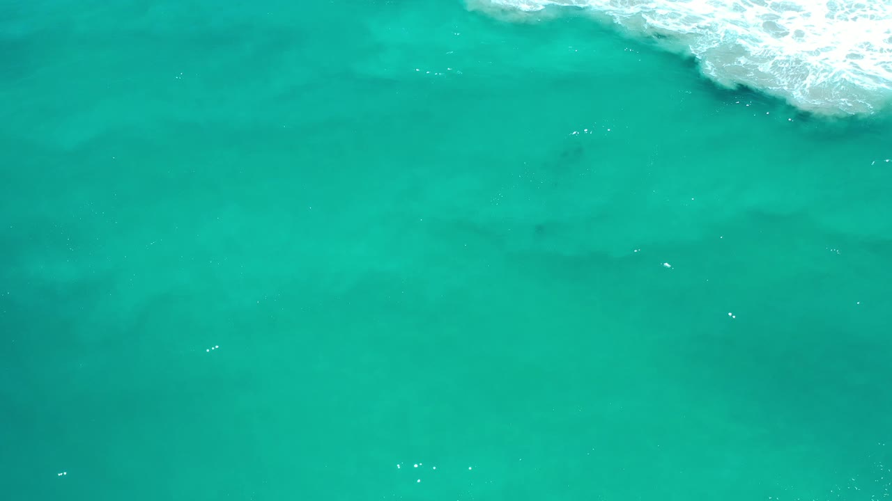 Clear teal ocean in Los Cabos, Mexico, fills the frame while foamy white water gathers near the top right, with no visible people.