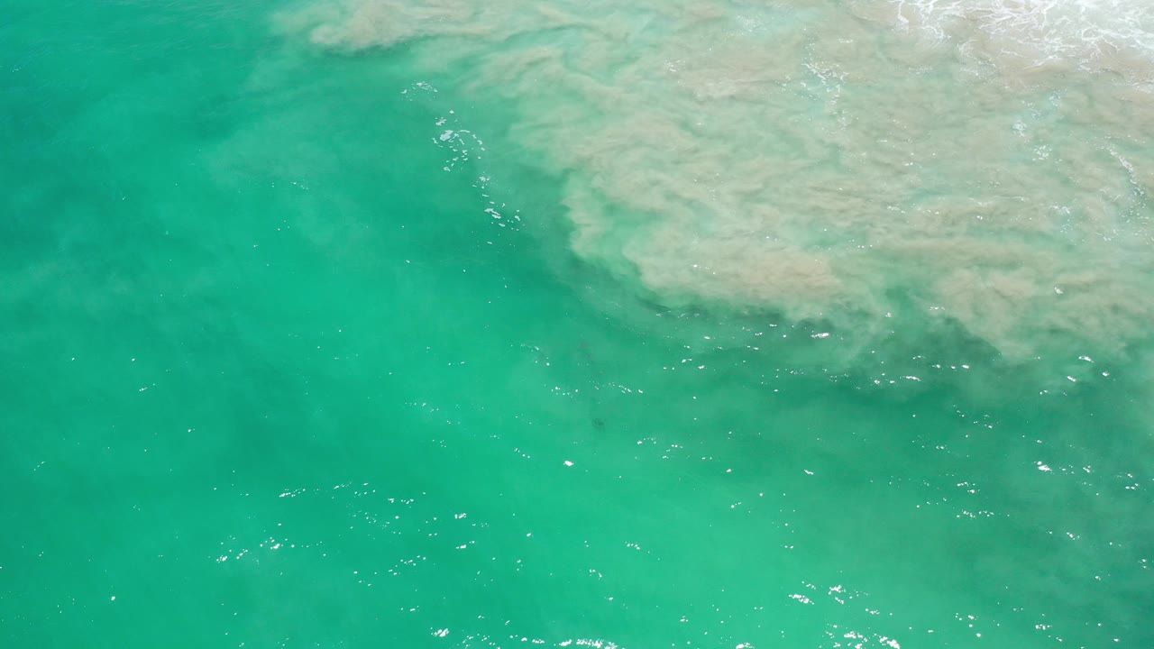 Overhead view of turquoise ocean water in Los Cabos, Mexico, with a pale submerged shelf entering from the upper right and no visible people.