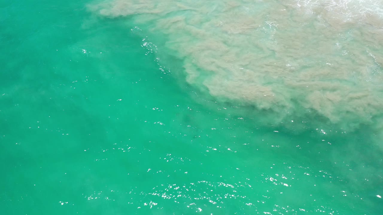 Aerial ocean surface with bright sparkles and sandy shallows