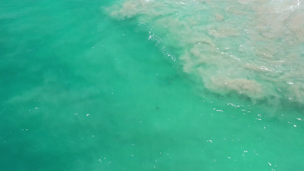 Overhead view of turquoise ocean water in Los Cabos, Mexico, with pale submerged wave or sand patterns near the top right and no visible people.