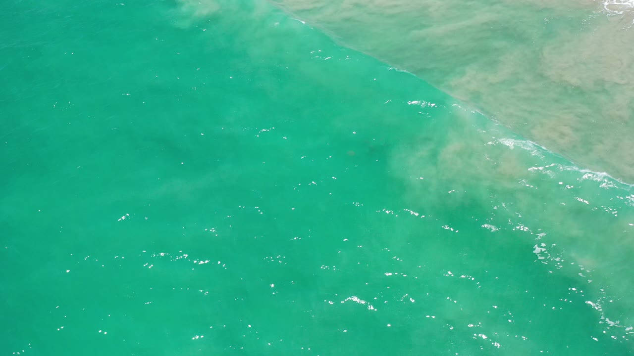 Top-down view of turquoise sea off Los Cabos, Mexico, with pale sandy shallows across the upper edge and no visible people.