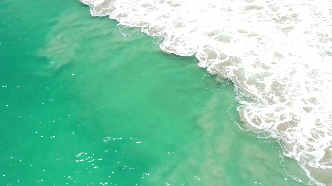 Turquoise water with bright surf foam across the upper right corner.