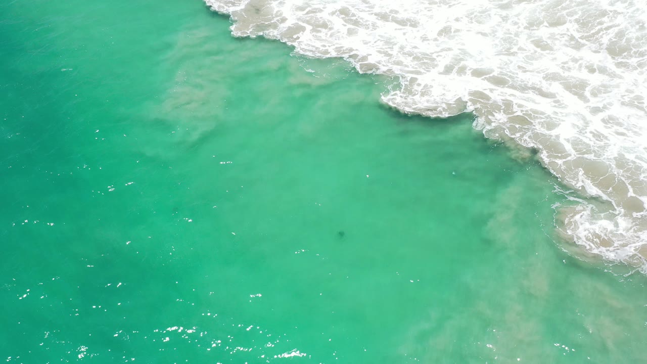 Turquoise ocean water with white surf entering from the upper right.
