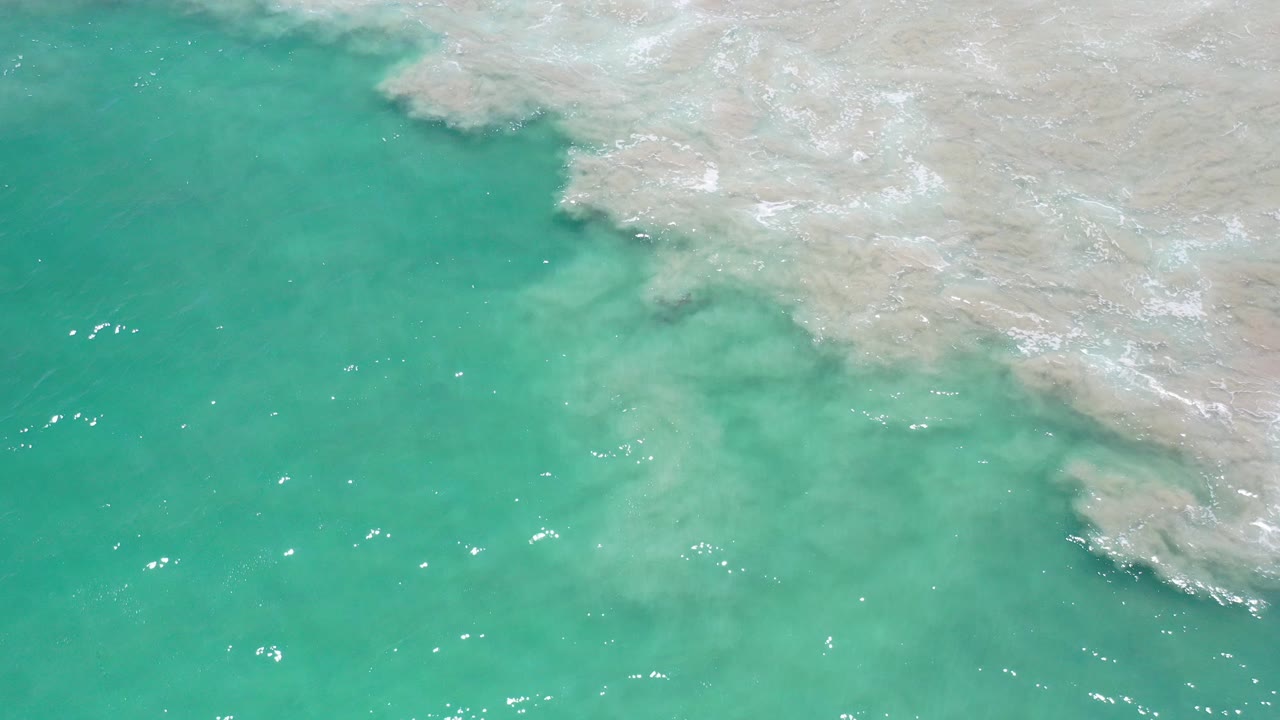 Turquoise water beside pale submerged rock and foam.