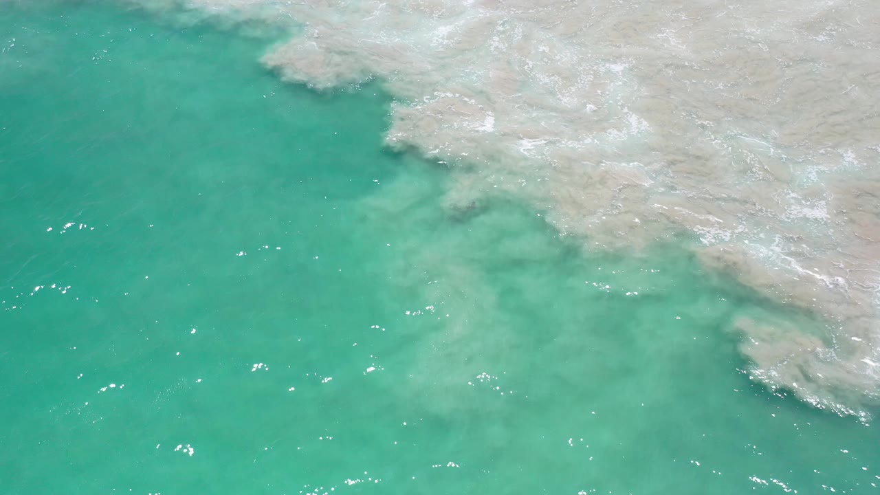 Aerial-looking frame of blue-green ocean in Los Cabos, Mexico, with a pale reef edge across the top and no visible people.