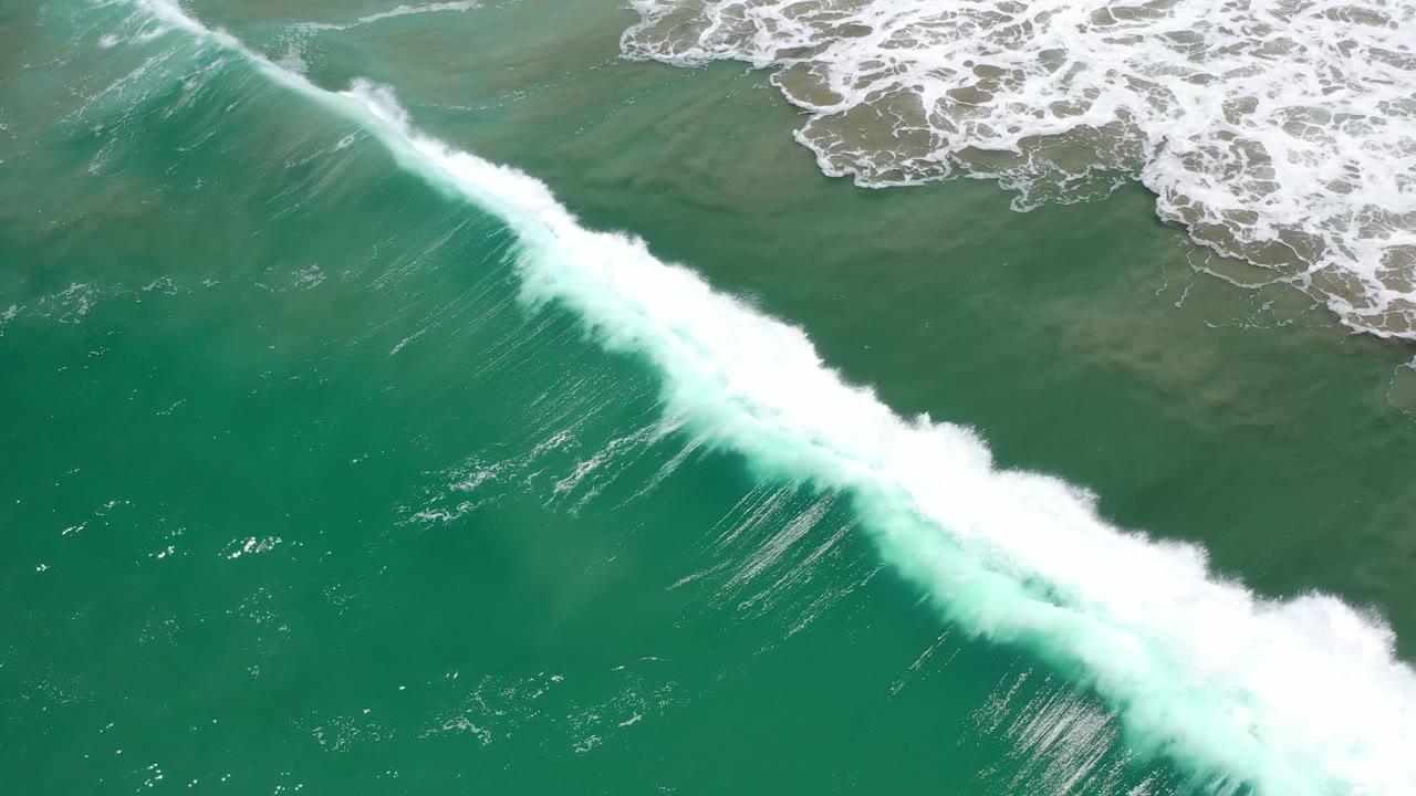 Breaking wave with white foam spreading over darker green water.