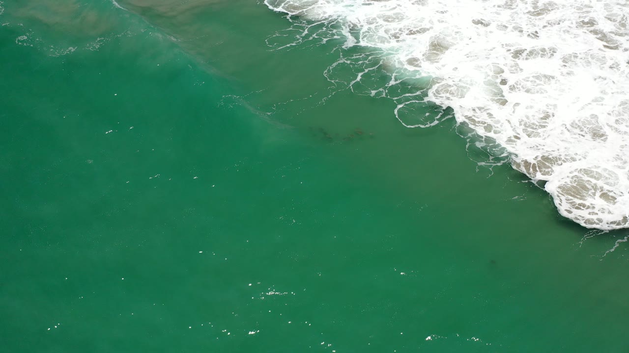 Green ocean water with white surf foam at the upper right.