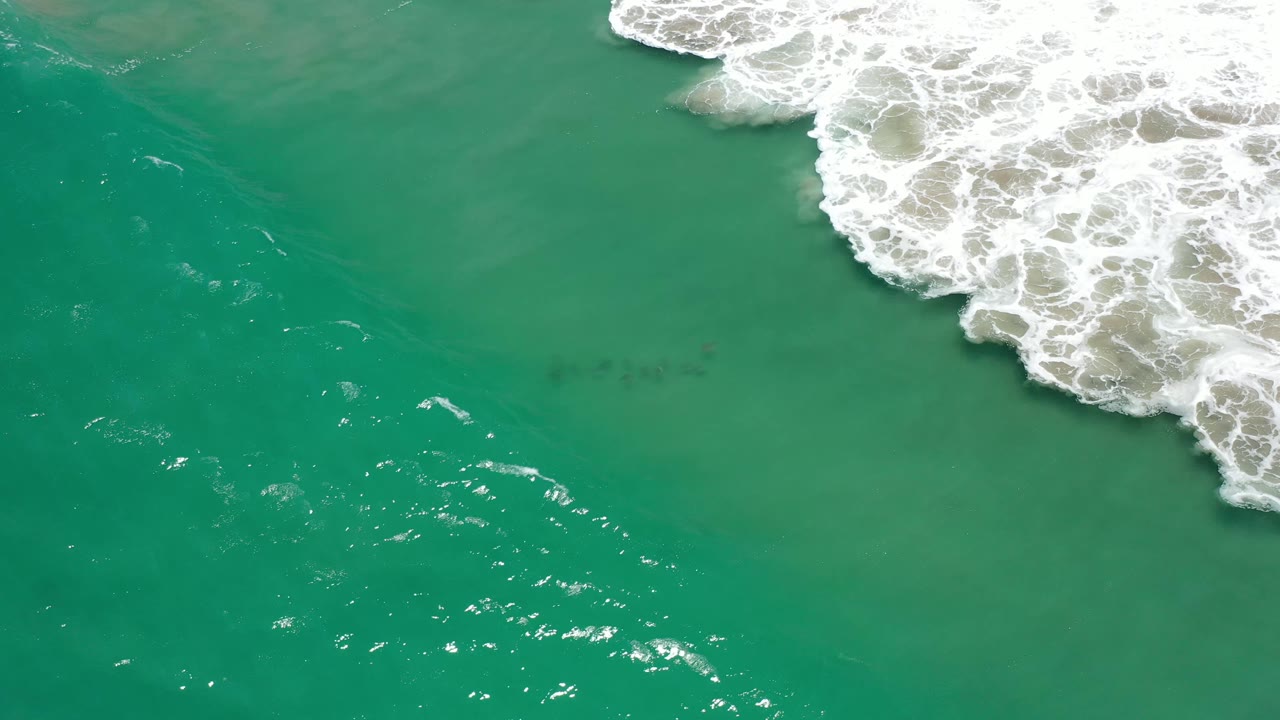 Aerial frame of Los Cabos green sea with white foam clustered at the upper right and open water across the lower half, no visible people.