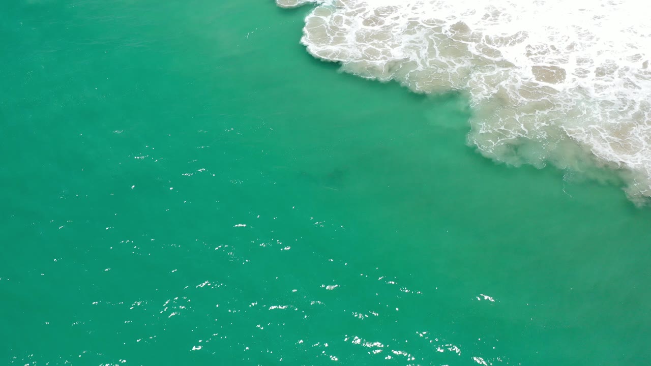 Turquoise ocean water with white surf foam at the upper right.