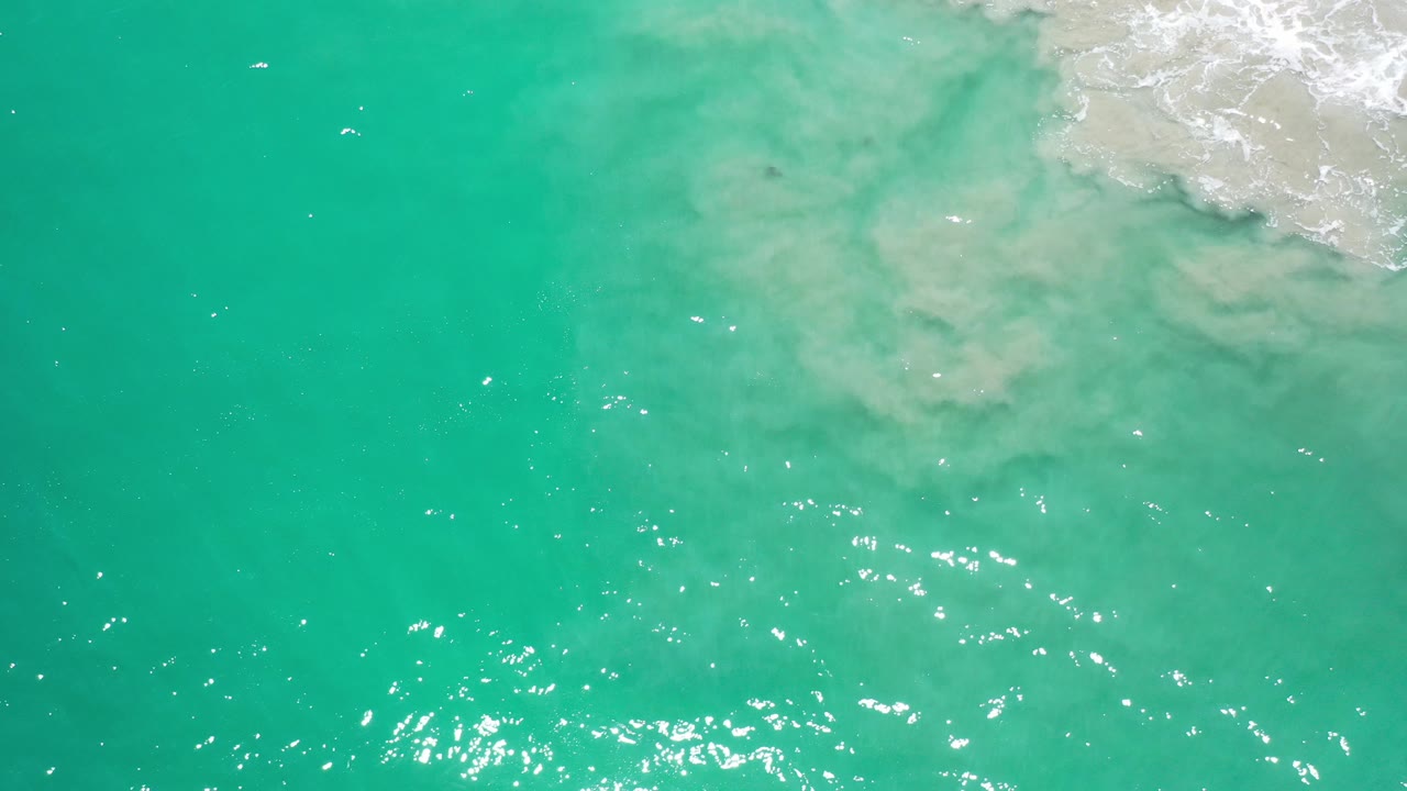 Overhead view of green-blue sea in Los Cabos, Mexico, with pale foam entering the upper right and no visible people.