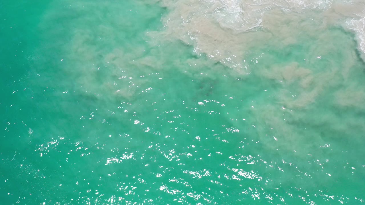Turquoise ocean water with pale surf churn at the top edge.