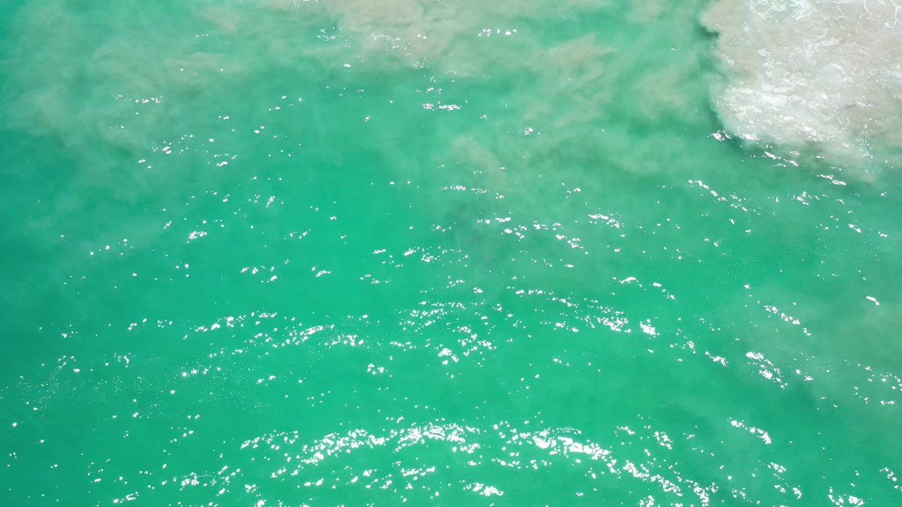 Turquoise-green ocean water with ripples and pale foam at the upper edge.