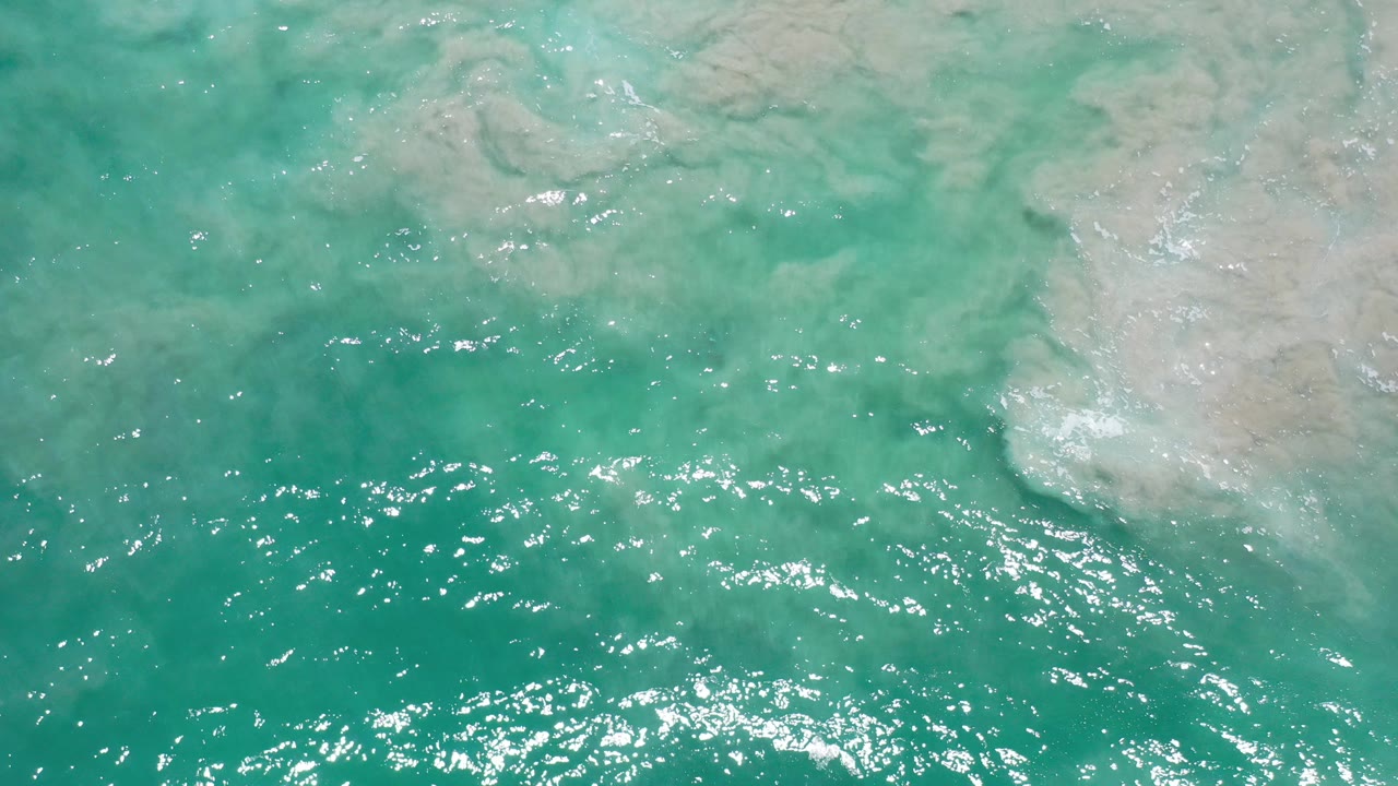Turquoise ocean water in Los Cabos, Mexico shows pale sandy rock shapes beneath surface ripples, with no visible people.