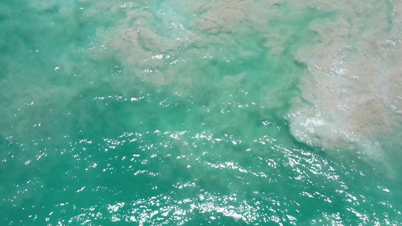 Green blue ocean water in Los Cabos, Mexico fills the frame as bright reflections gather across the lower half, with no visible people.
