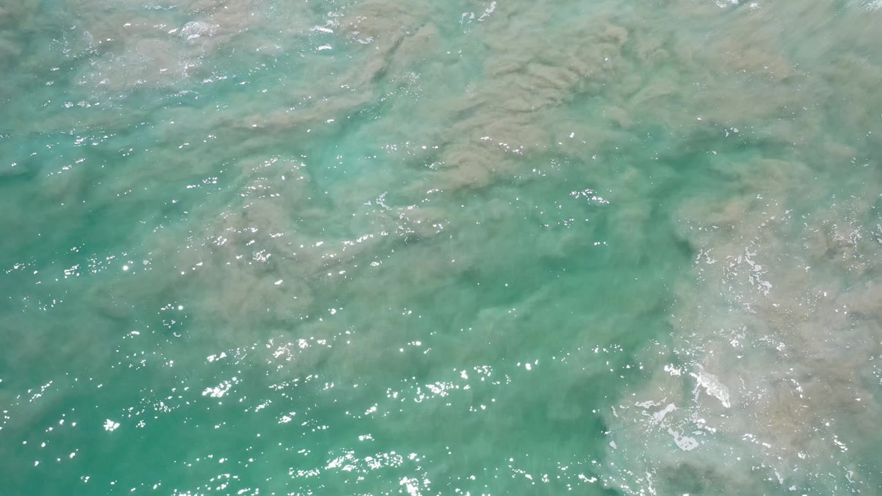 Green-blue shallow water in Los Cabos, Mexico ripples over cloudy beige sand bands, with no visible people.
