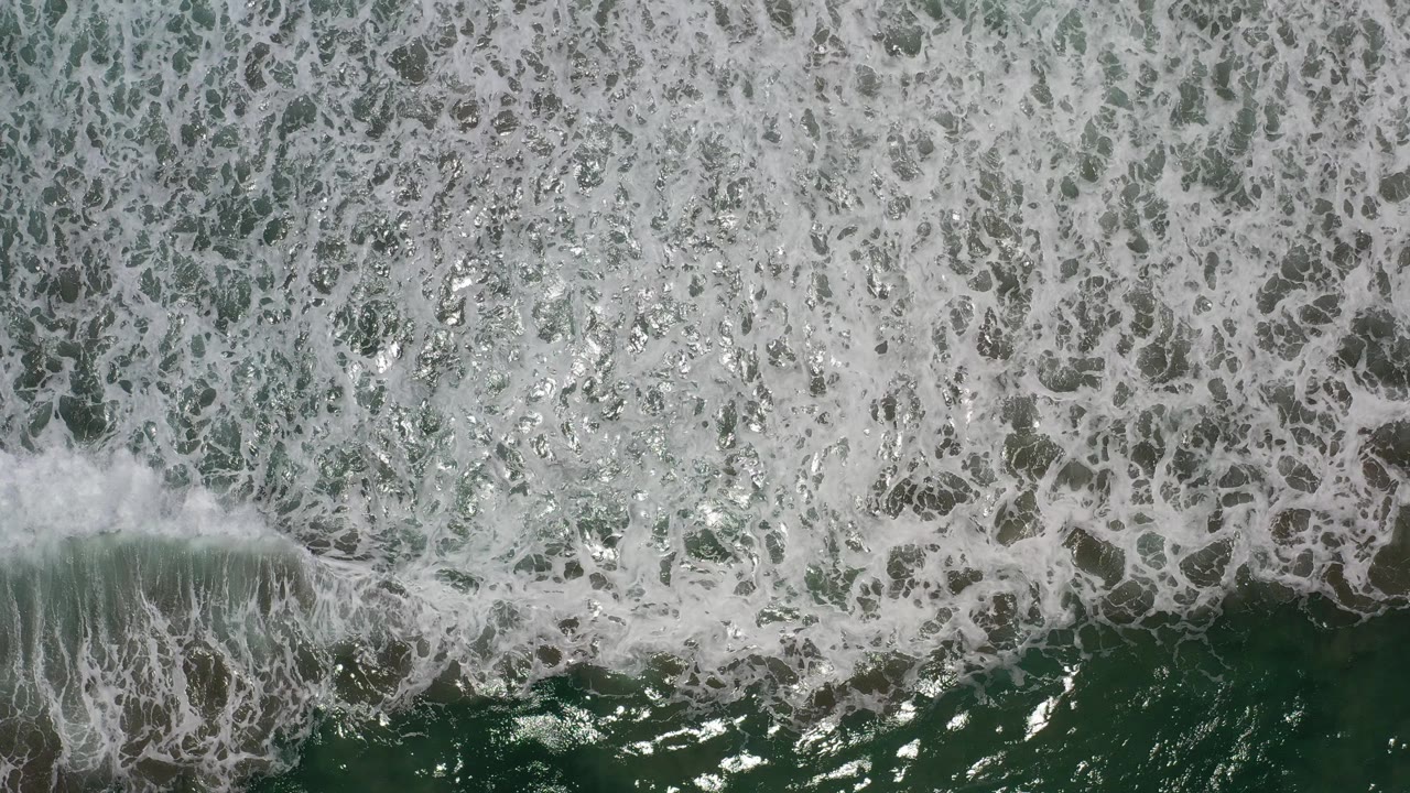 Overhead view of foamy green-blue surf in Los Cabos, Mexico, with bright water highlights and no visible people.