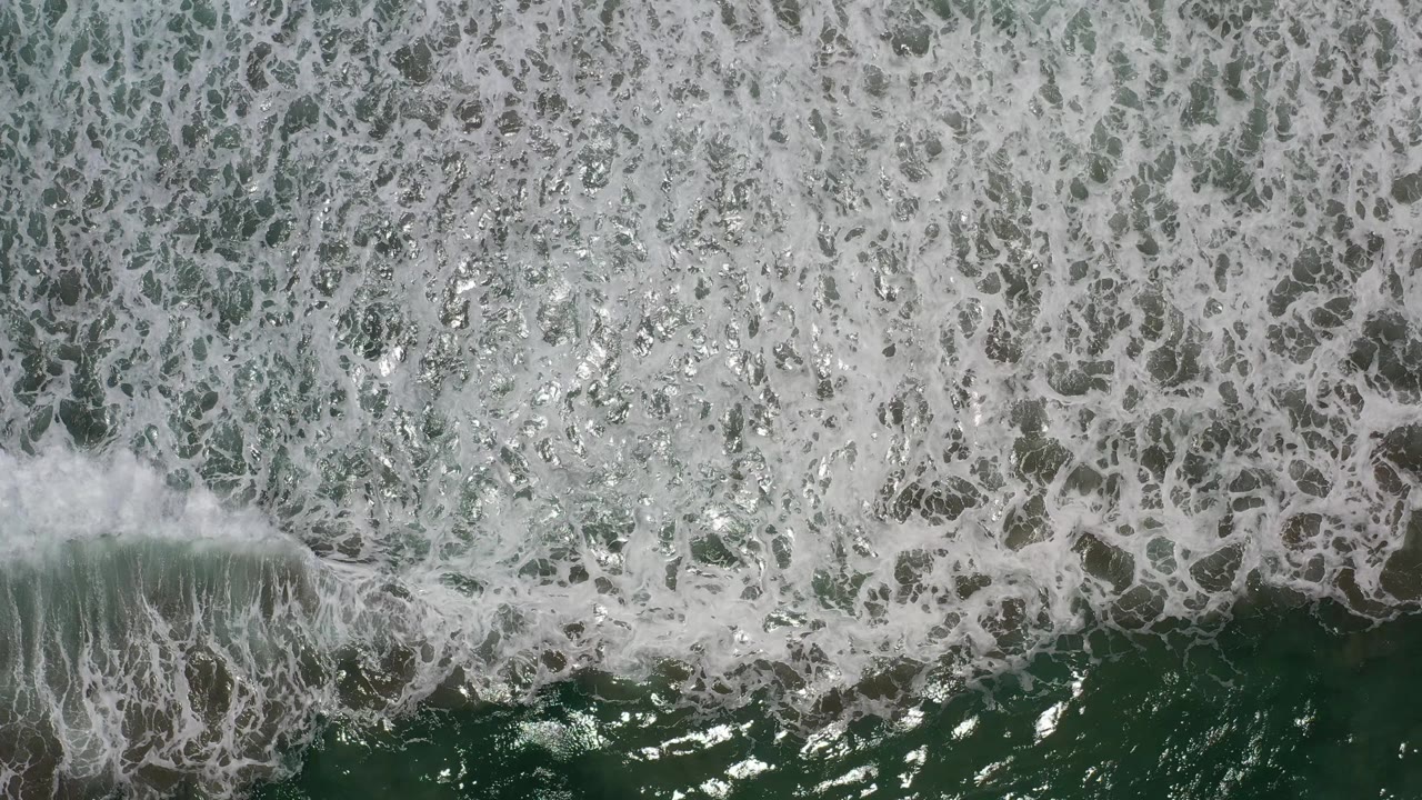 A white breaking wave cuts across green-blue water in Los Cabos, Mexico, with no shore visible and no visible people.