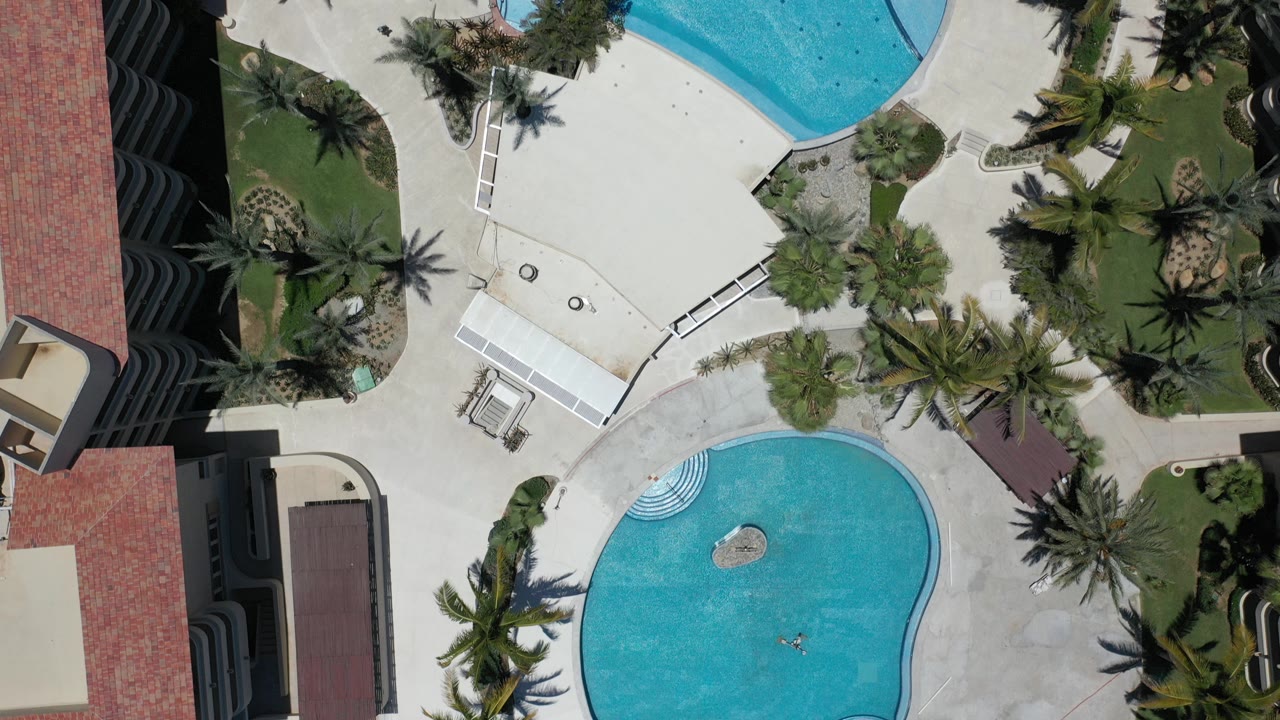 Overhead resort pools, palm trees, lawns, and red tile roof edges.
