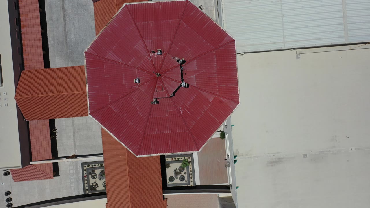 Top-down view of red roof sections beside pale rooftops.