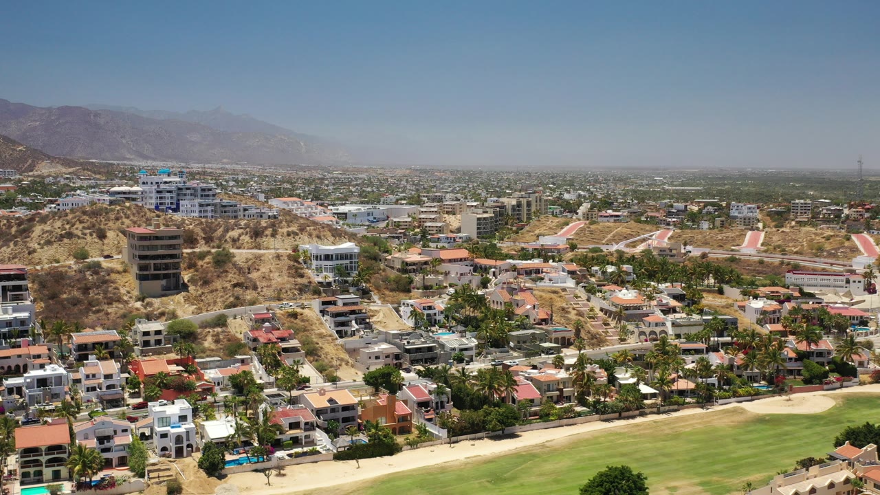 Aerial view of hillside homes, green fairway, and distant mountains.