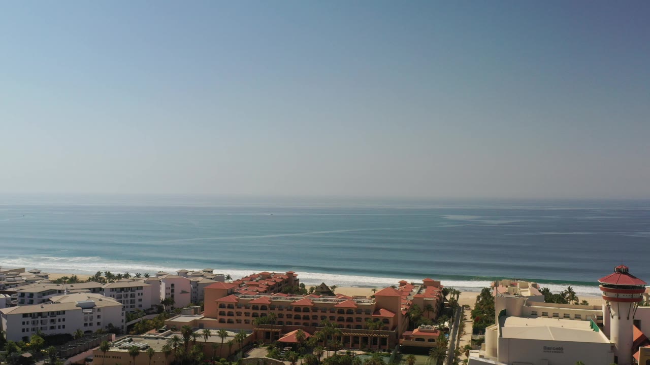 Wide coastal view with ocean, surf, beach, and beachfront buildings.