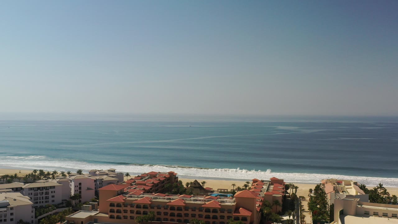 Aerial view of beachfront buildings, sandy shore, surf, and open ocean.