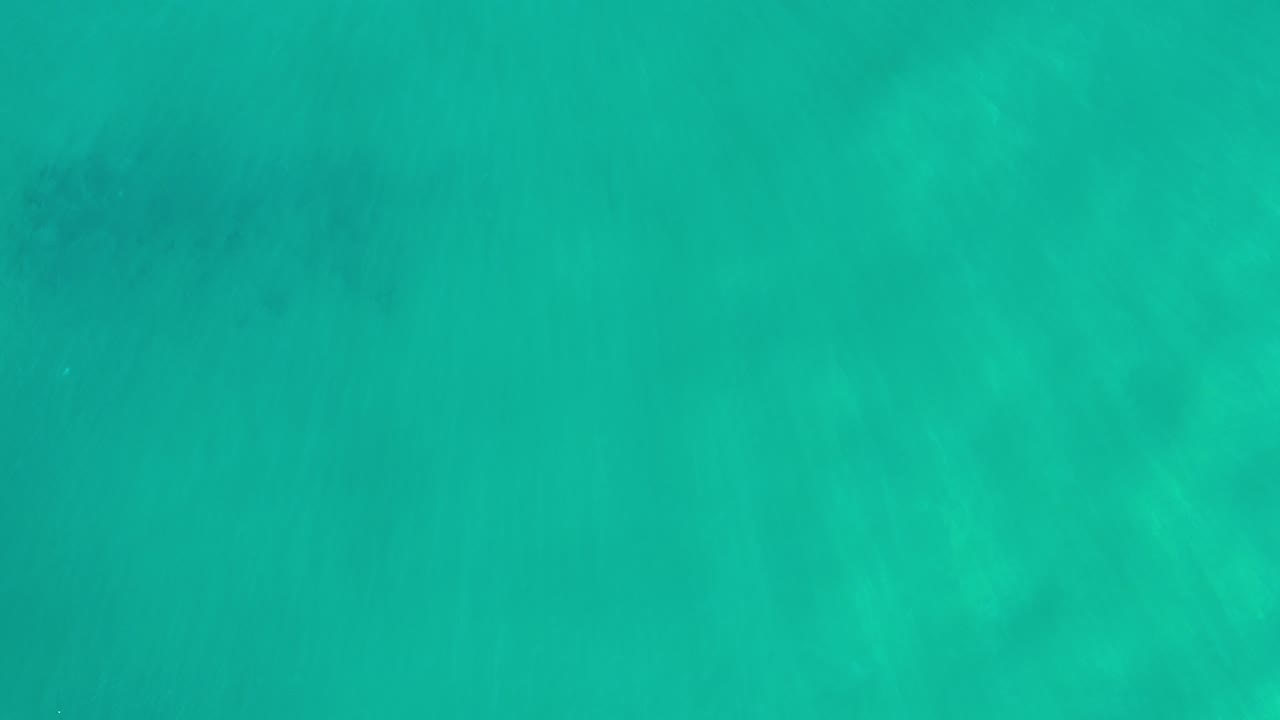 Overhead view of turquoise seawater in Los Cabos, Mexico, with pale ocean floor patterns showing through and no visible people.