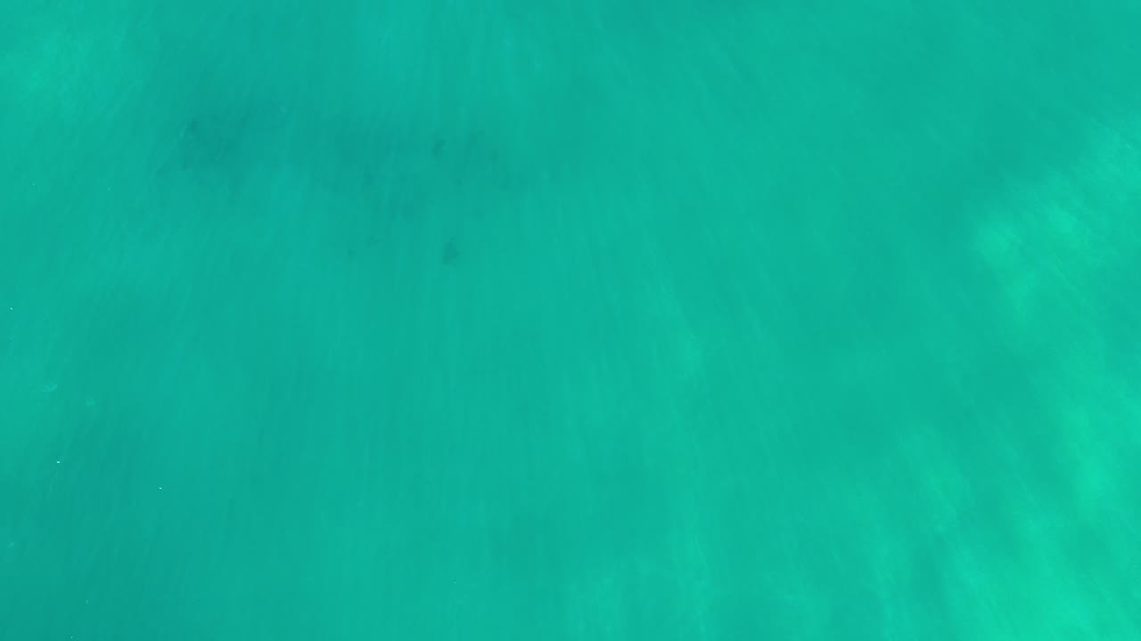 Overhead view of turquoise water in Los Cabos, Mexico, with faint darker patches under the surface and no visible people.