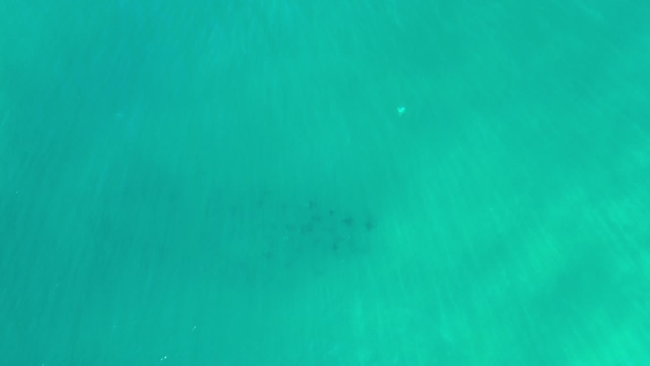 Overhead view of turquoise-green ocean water in Los Cabos, Mexico, with faint darker patches below the surface and no visible people.