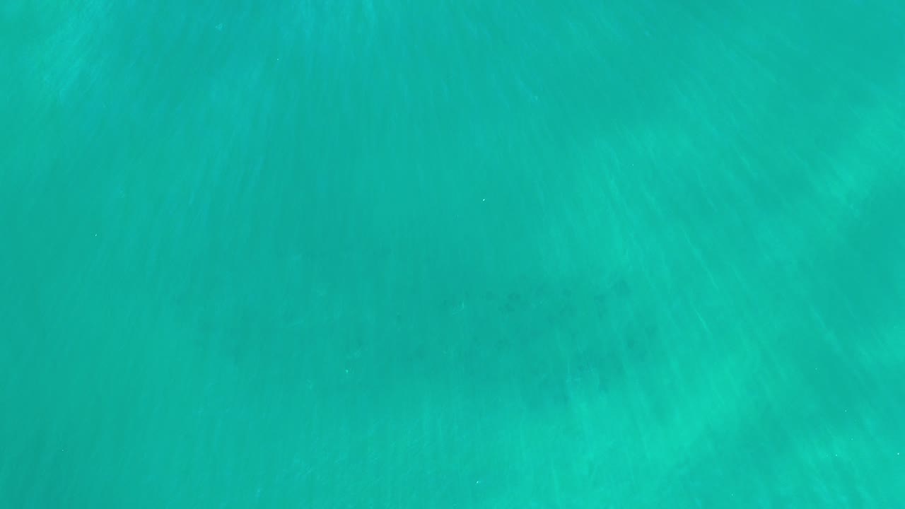 Overhead view of turquoise water in Los Cabos with pale underwater streaks and no visible people.