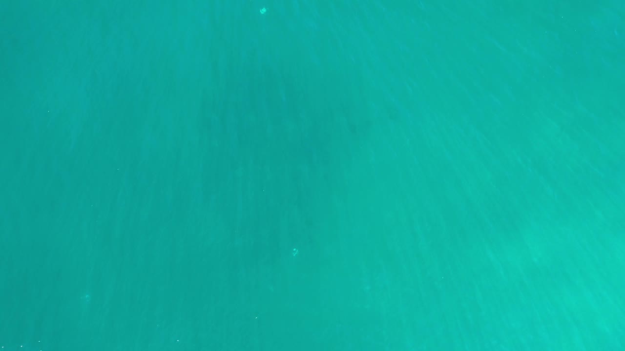 A high overhead frame of aquamarine Los Cabos water shows soft sand marks under the surface, with no visible people or boats.