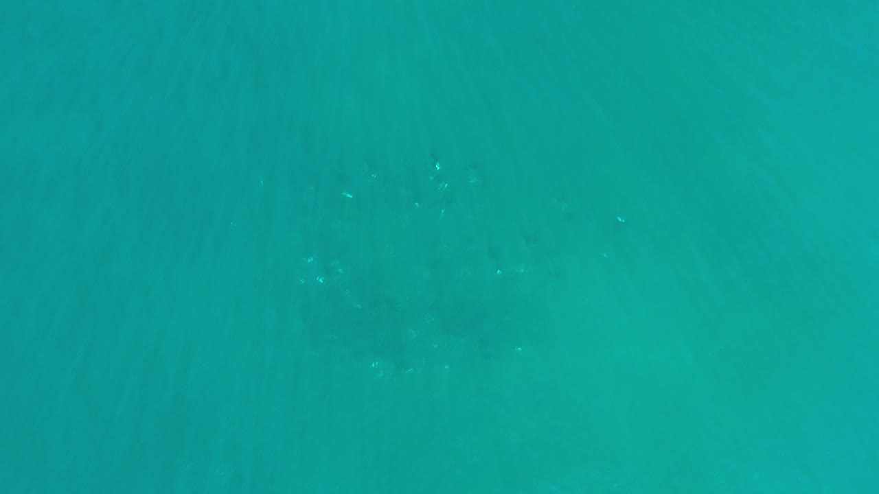 Turquoise ocean surface with darker patches below and small points of reflected light.