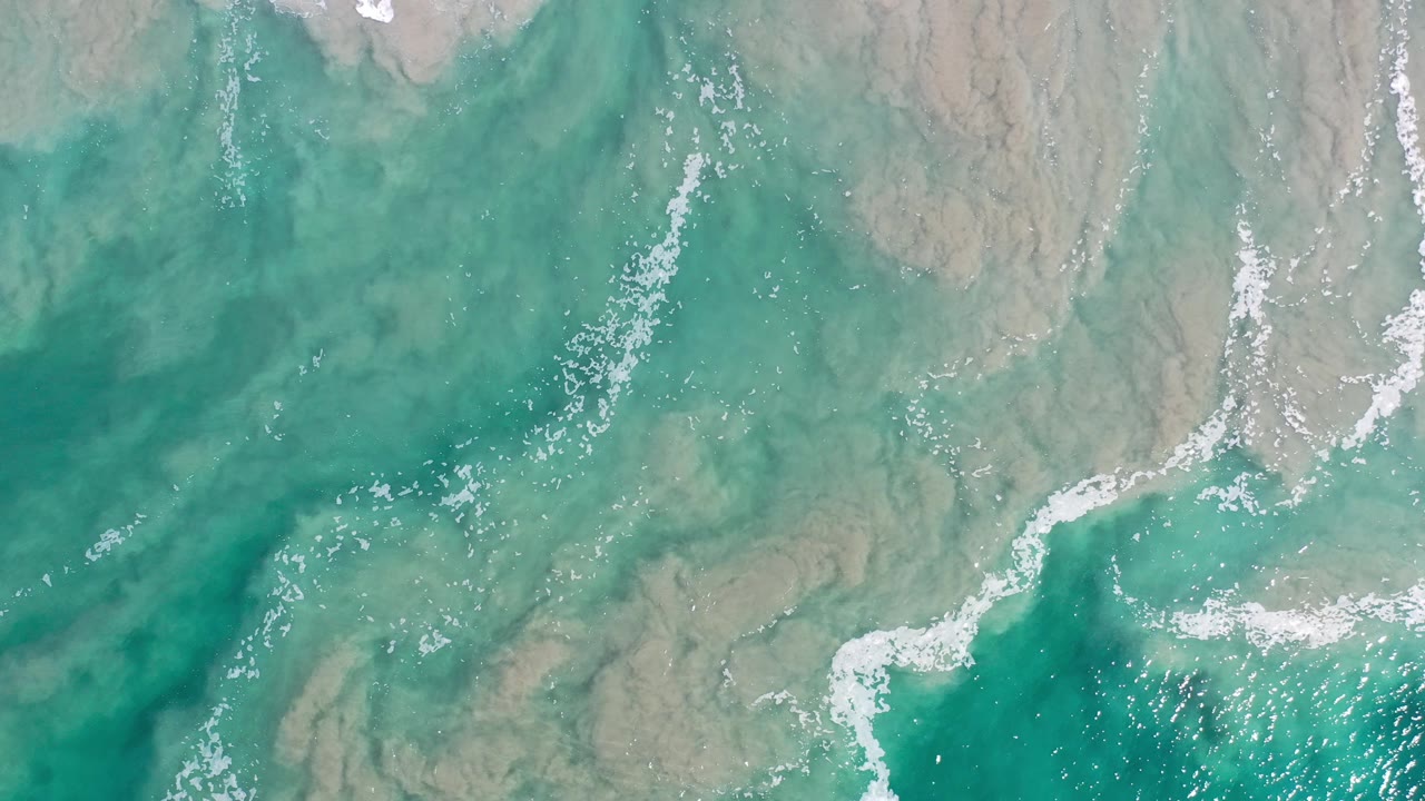 Green ocean shallows with white foam curves and sandy texture
