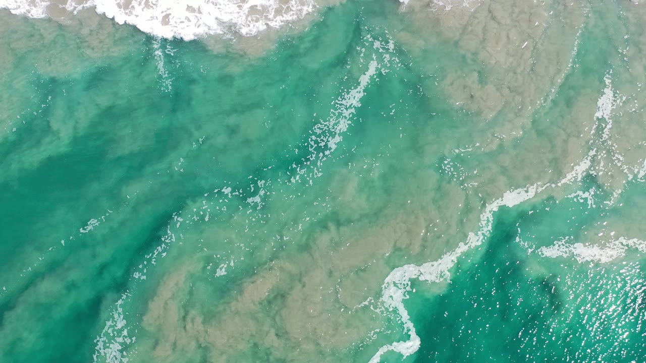 Overhead surf foam over pale green shallows