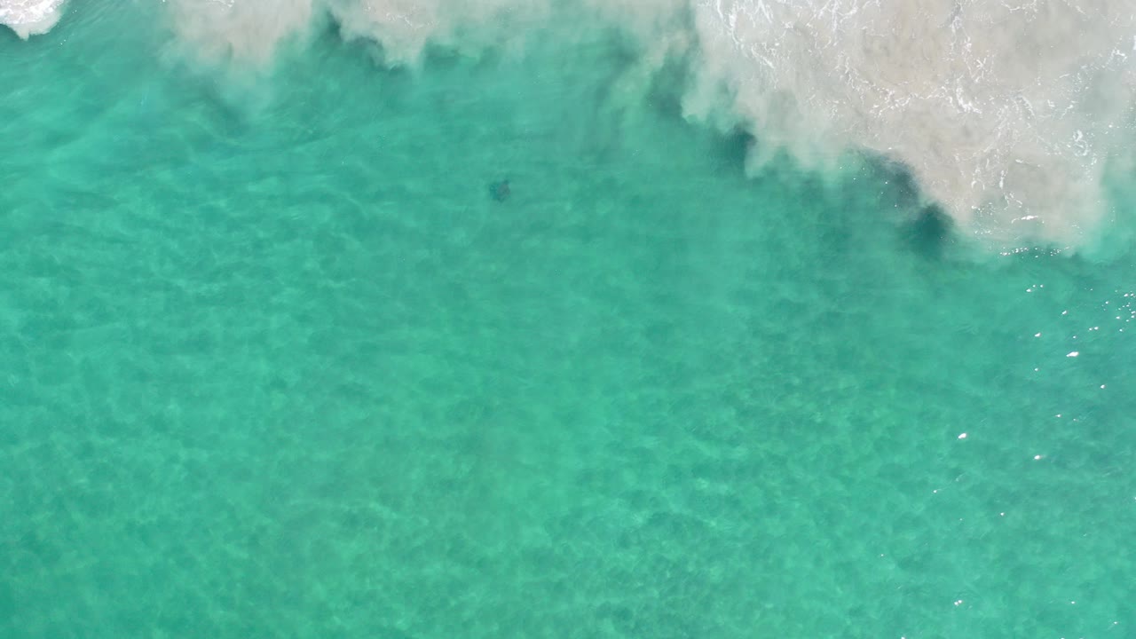 Top-down view of green sea in Los Cabos, Mexico, with white surf foam pushing in from the upper edge and no visible people.