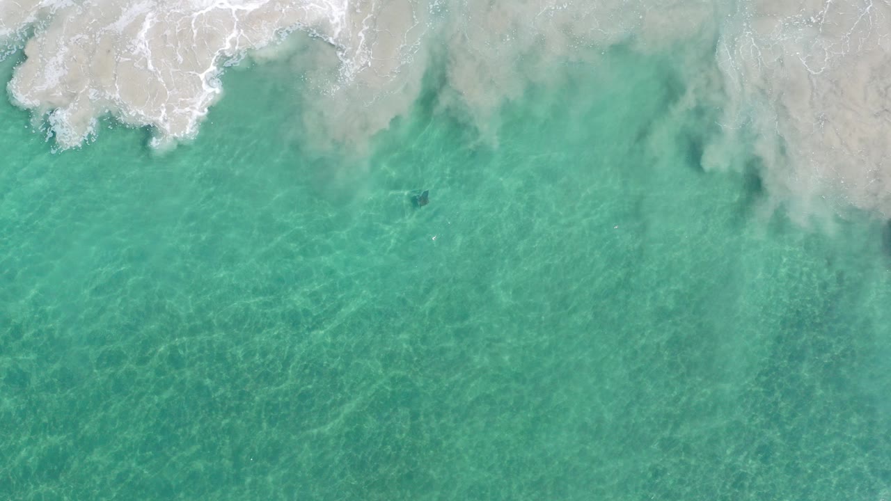 Overhead turquoise water with white surf at the sandy shore.