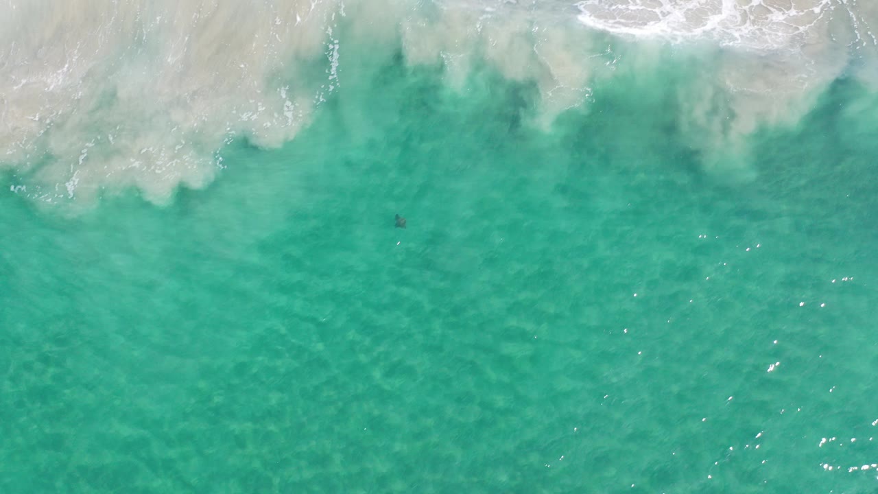 Overhead view of turquoise ocean water in Los Cabos, Mexico, with a band of white surf entering from the top edge and no visible people.