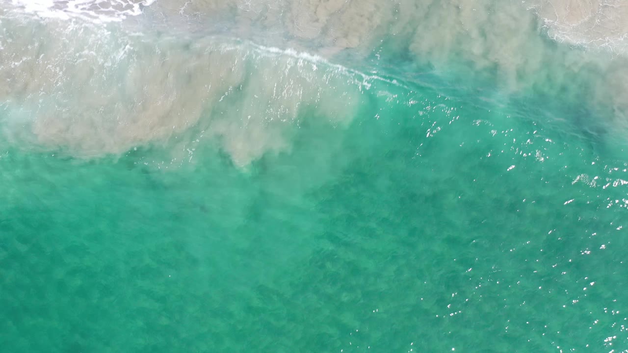 Translucent green-blue sea in Los Cabos, Mexico, with foam drifting across the upper edge and no visible people or objects.