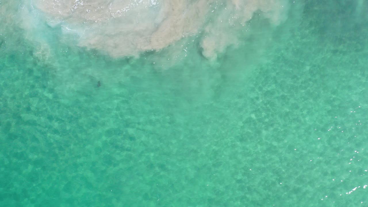 Overhead view of turquoise seawater in Los Cabos, Mexico, with pale submerged rock or sand along the top edge and no visible people.