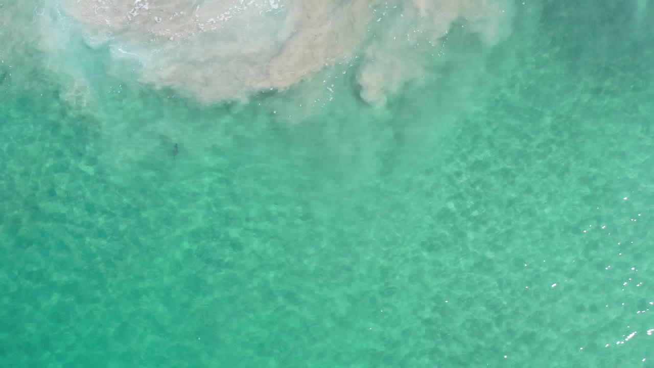 Clear green-blue seawater fills the frame in Los Cabos, Mexico, with a pale submerged formation near the top and no visible people.