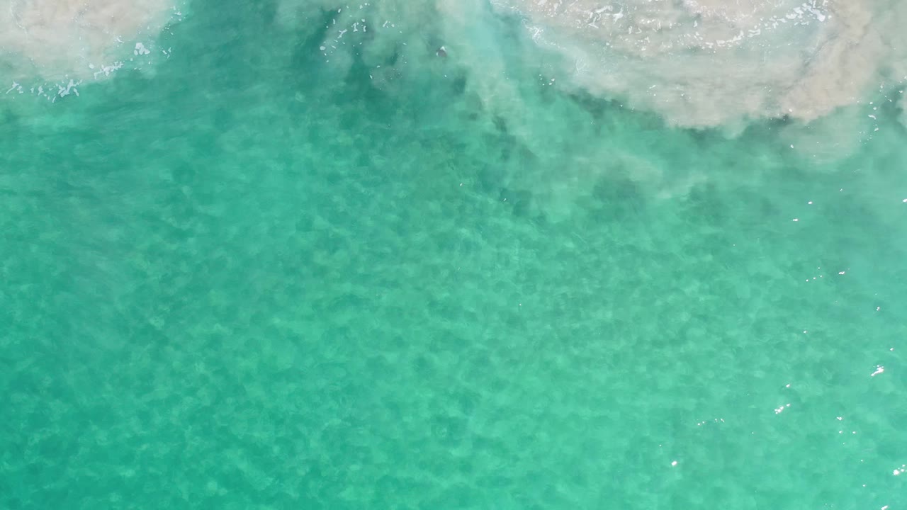 Top-down Los Cabos ocean frame with clear turquoise water, pale sand clouding under the surface, and no visible people.