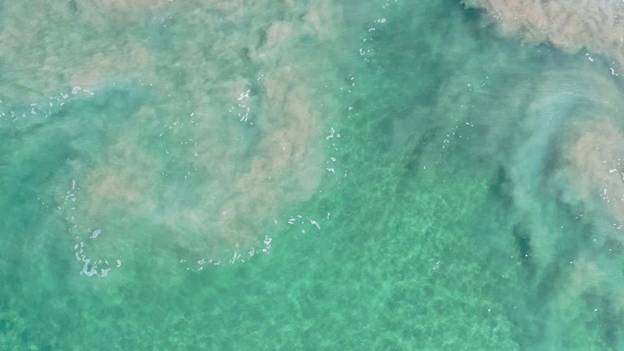 Overhead turquoise ocean water in Los Cabos, Mexico, with pale cloudy wave wash near the upper frame and no visible people.