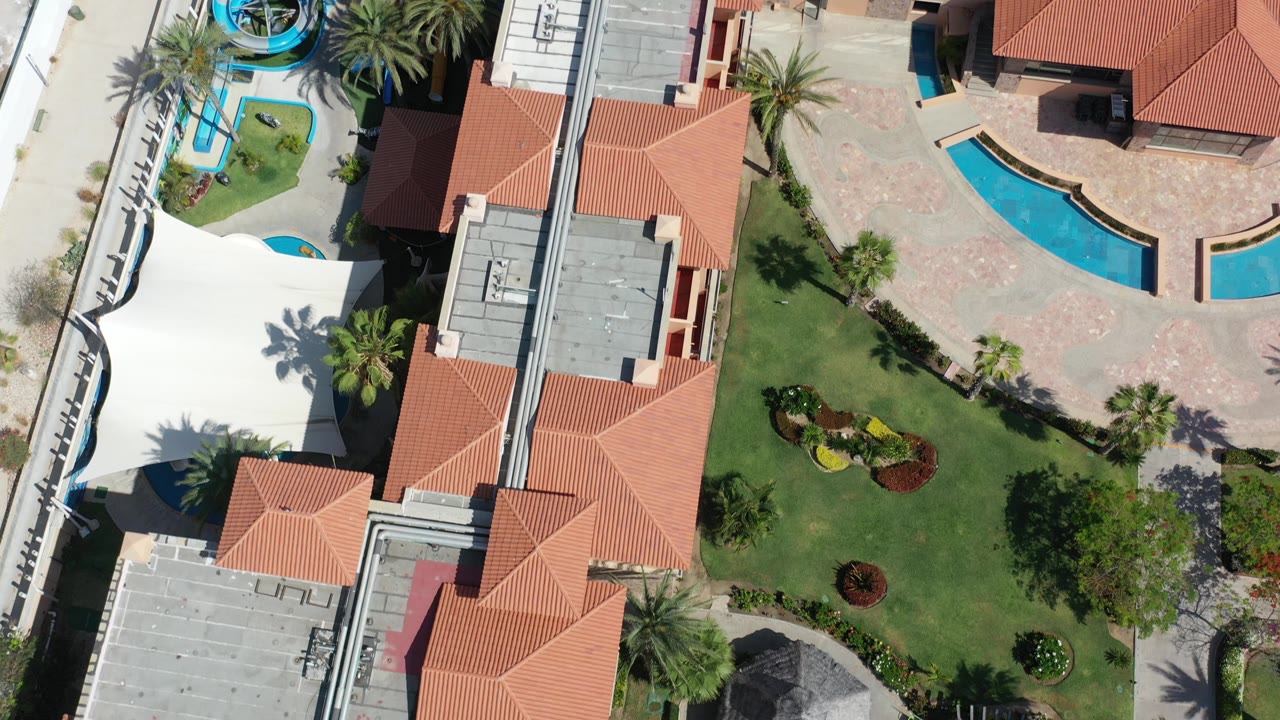 Aerial view of roofs, lawns, pools, palms, and a water slide area.