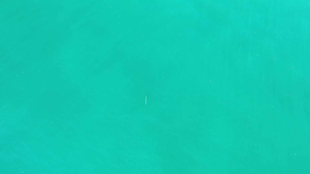 Turquoise blue-green water surface in Los Cabos, Mexico with faint ripples, a tiny pale floating mark near the upper area, and no visible people.