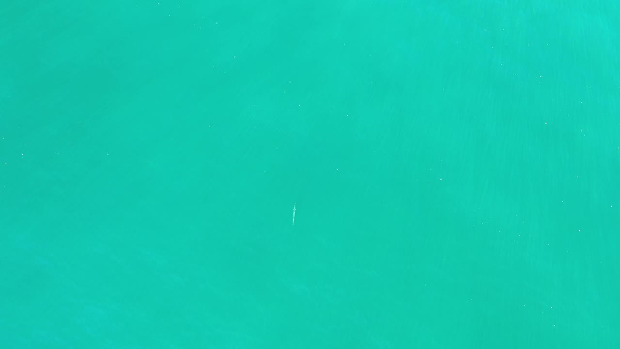 Aerial frame of teal open water in Los Cabos, Mexico, with mist softening the surface and no visible people.
